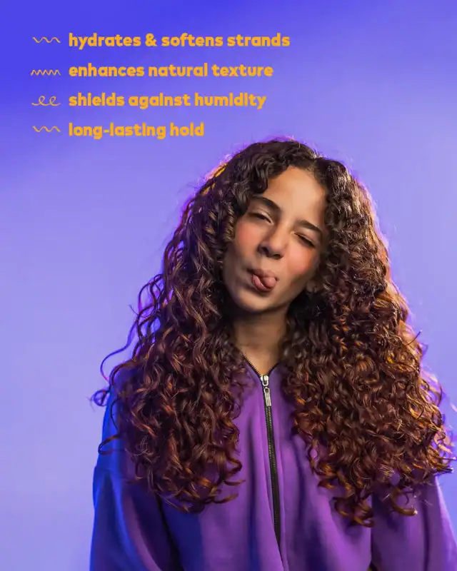 Twist-out curly hair natural hairstyle woman with long, voluminous curls wearing a purple hoodie smiling against purple background.