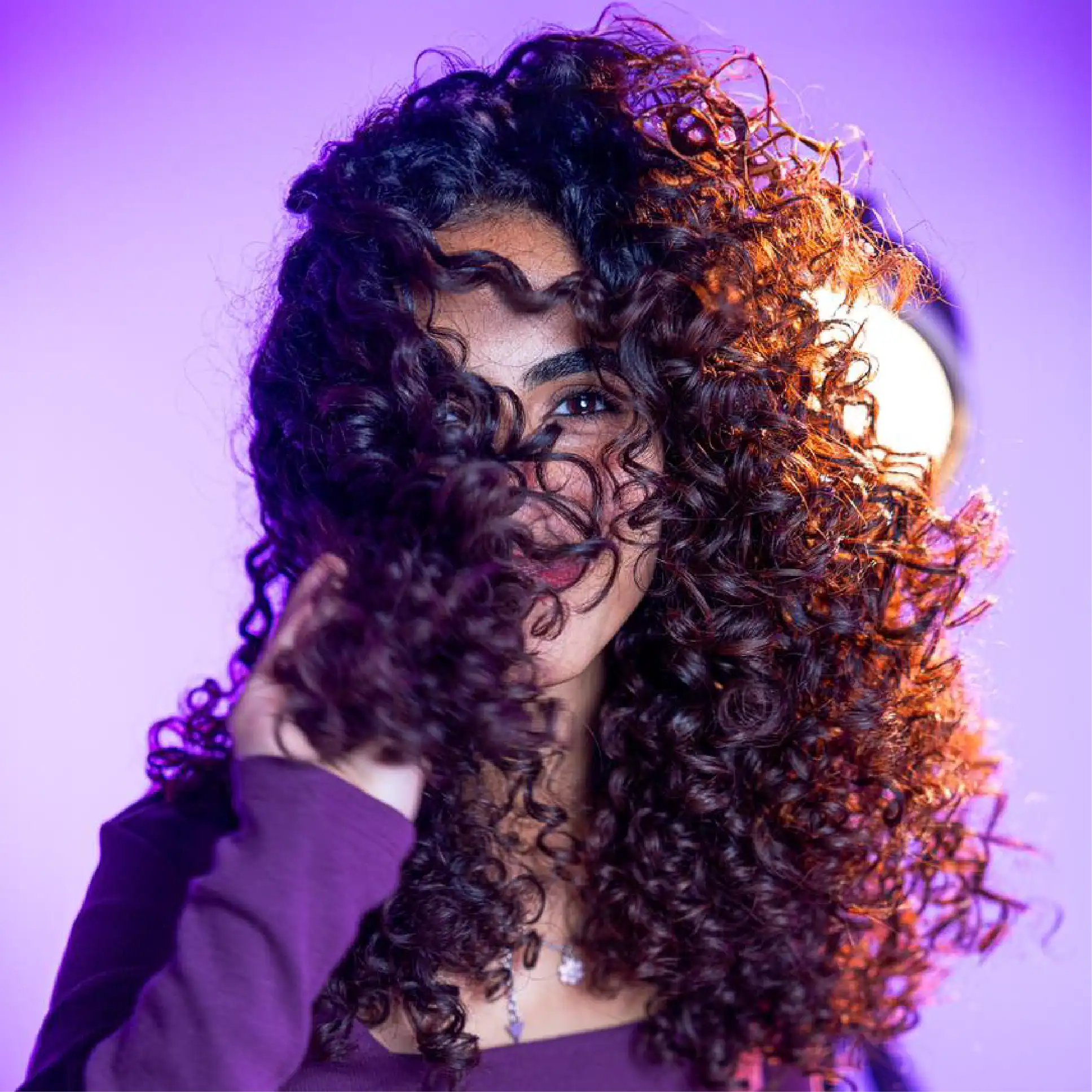 Vibrant curly hair woman with dark roots and copper highlighting, showcasing healthy, defined curls, perfect for curly hair care inspiration and beauty products from Curlit.