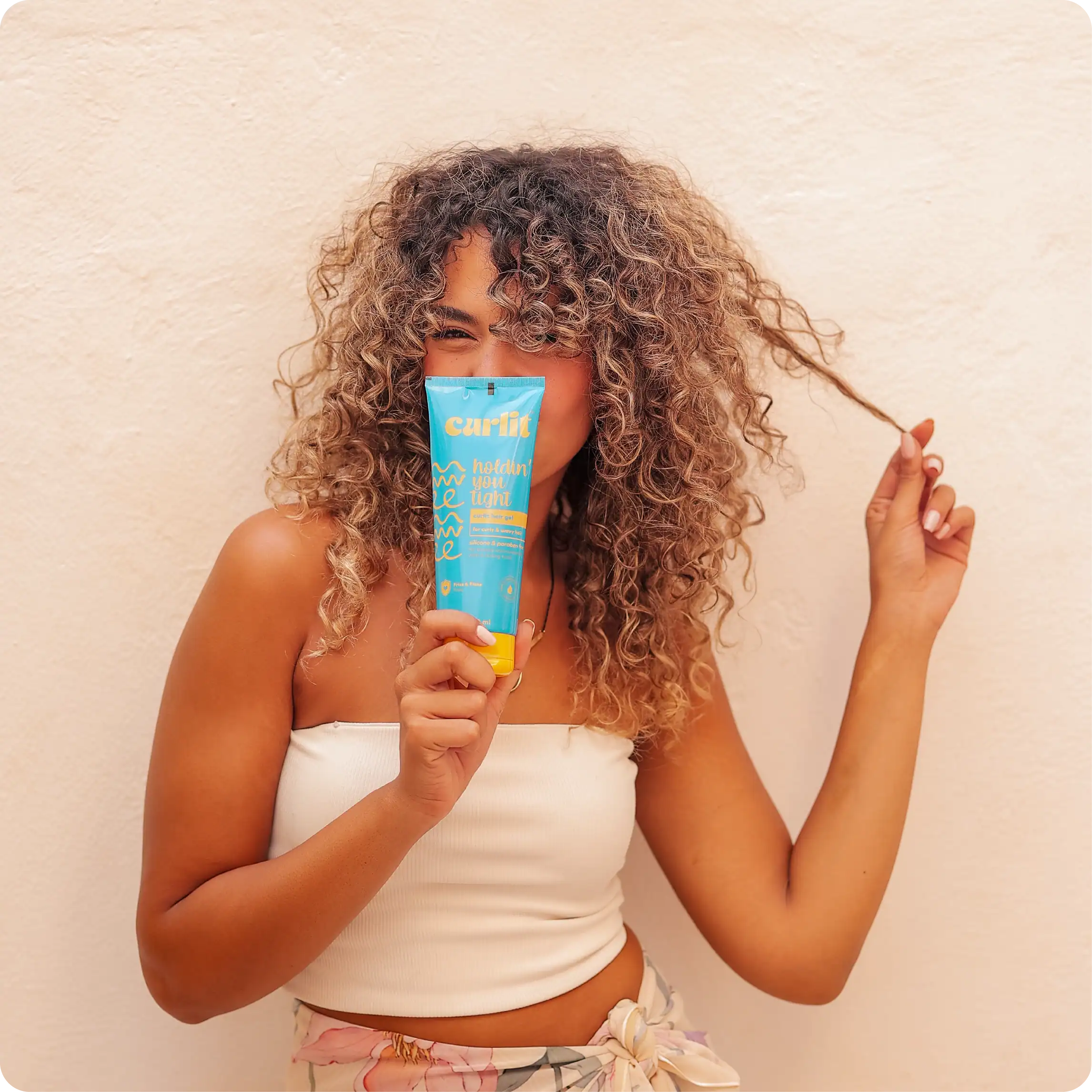 Silky curly hair woman holding Curlit hair product, happy with her textured hairstyle, demonstrating curly hair care routine, natural hair styling, and hair product for curls.