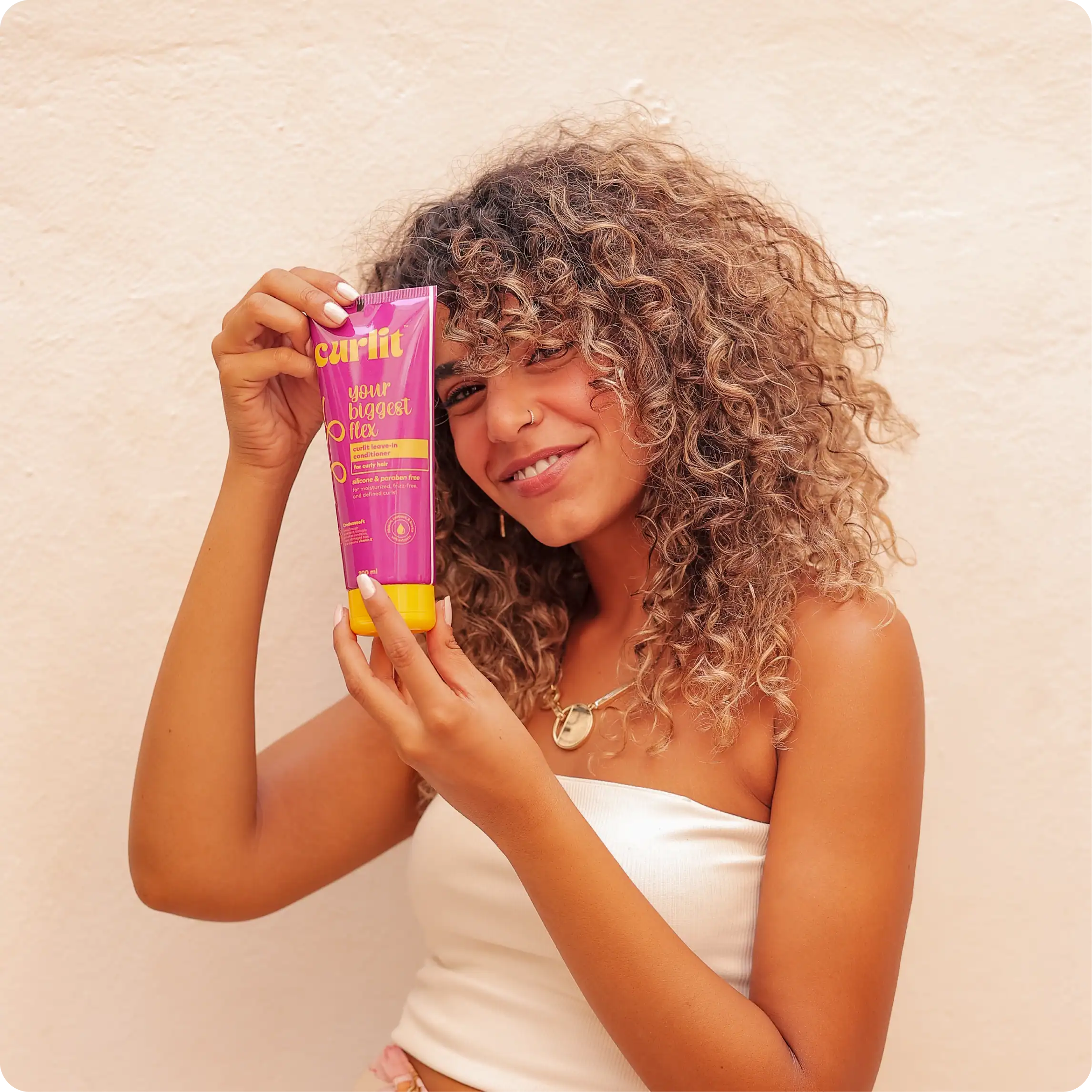 Vibrant woman with curly hair holding Curlit hair product, showcasing a natural hairstyle, emphasizing curl definition and hair care essentials for curly hair.