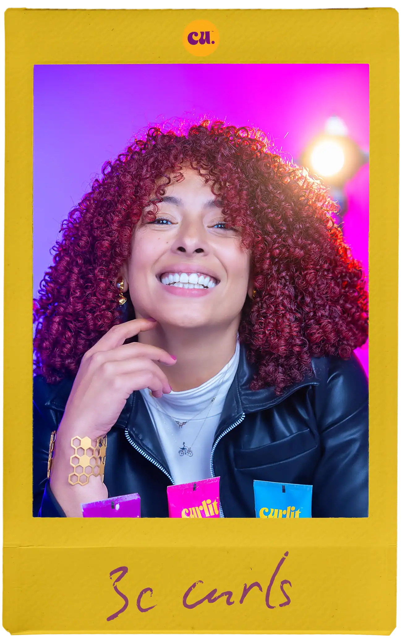 Vibrant red curly hair woman smiling with colorful curling products on pink and purple background.