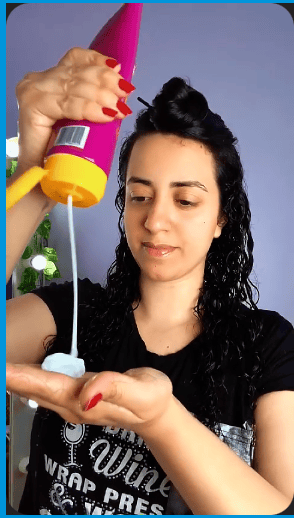 Vibrant curl cream being applied to black curly hair for defining and styling curls with a curling tool in the background.
